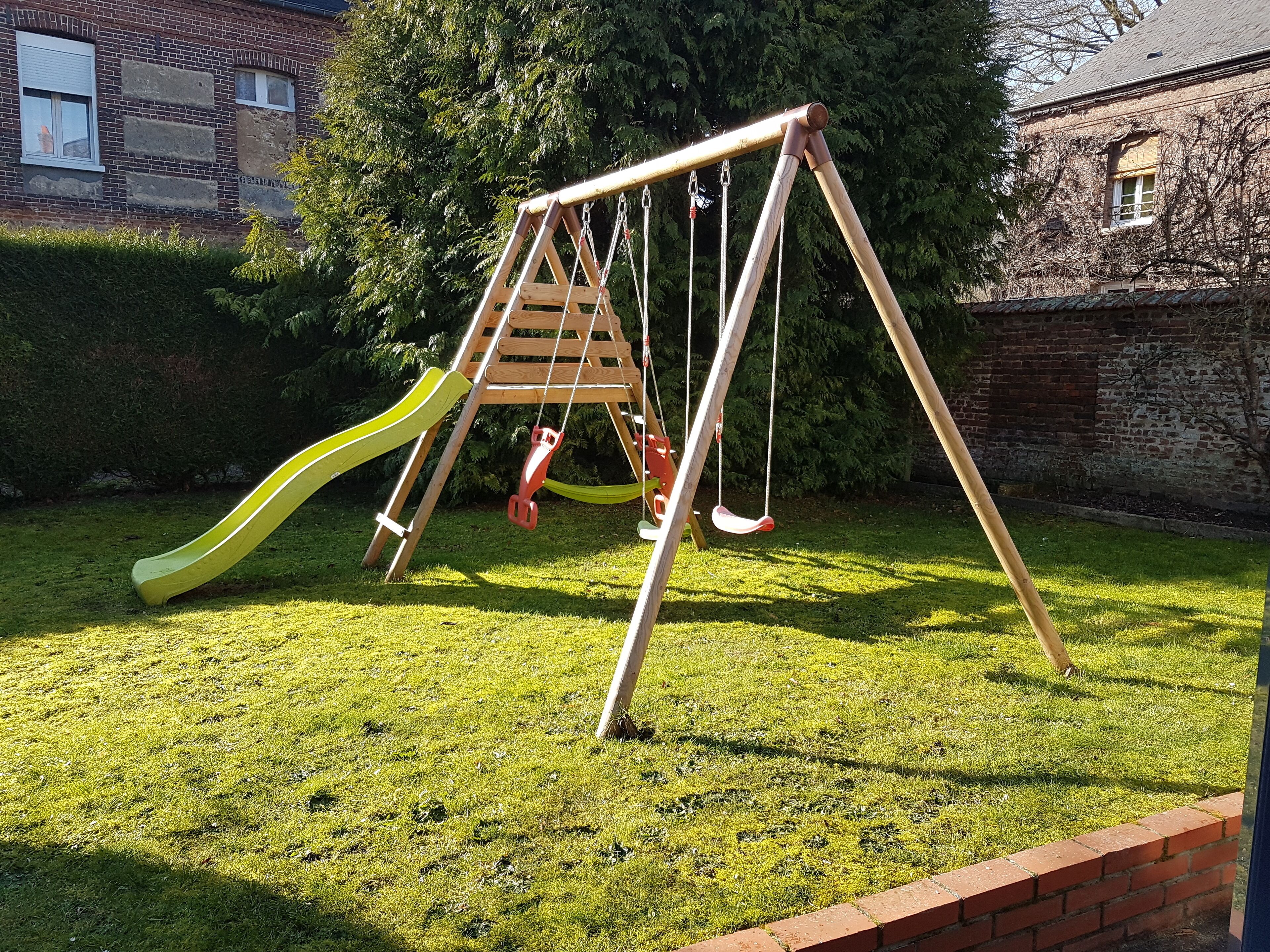 A wooden swing set with two swings and a yellow slide in a grassy yard.