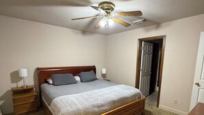 Una camera da letto con un letto in legno, una ventola a soffitto, un comodino, una lampada e una porta.
