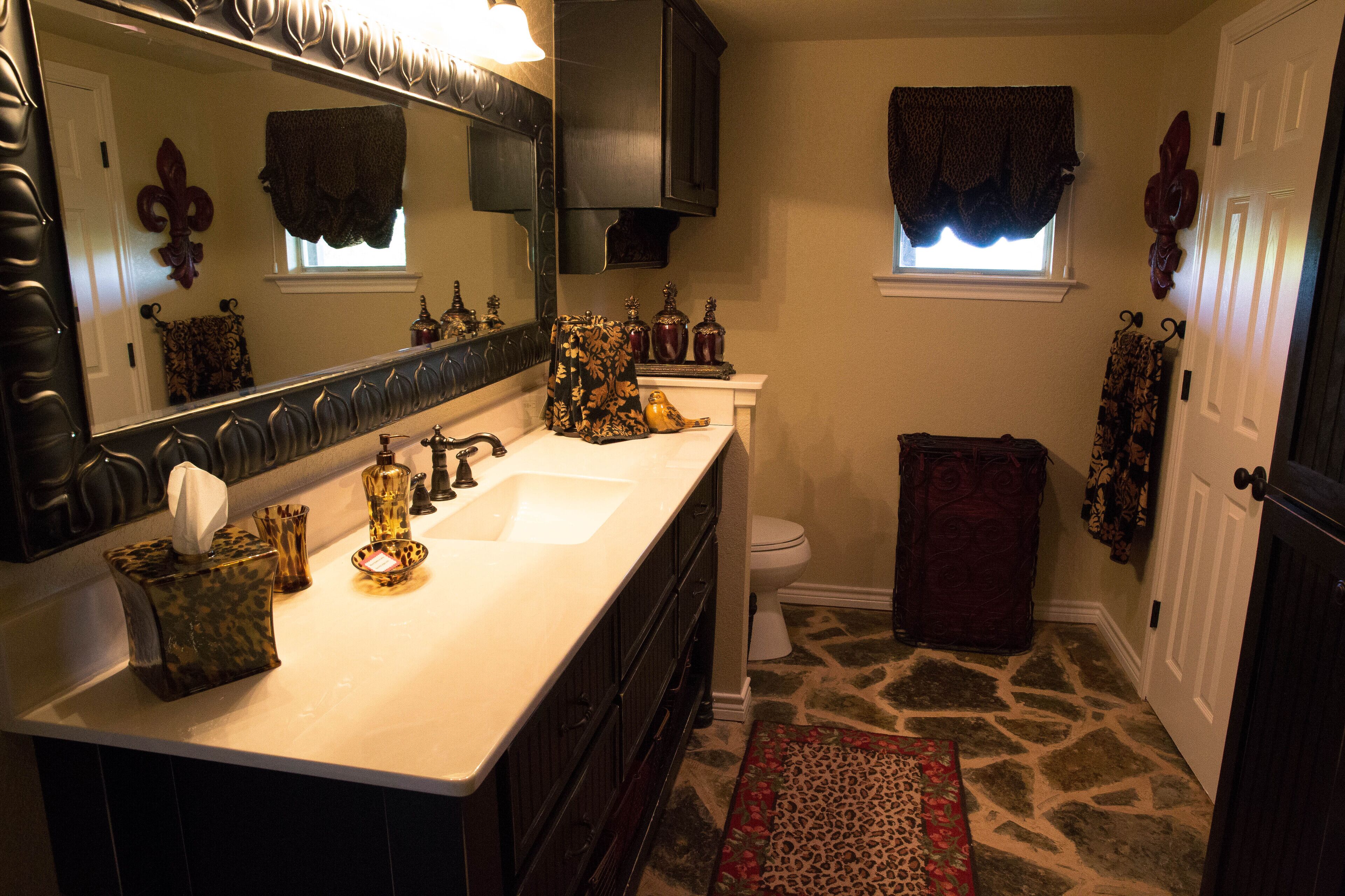 A bathroom with a white sink, dark cabinets, a large mirror, a toilet, and a patterned rug.