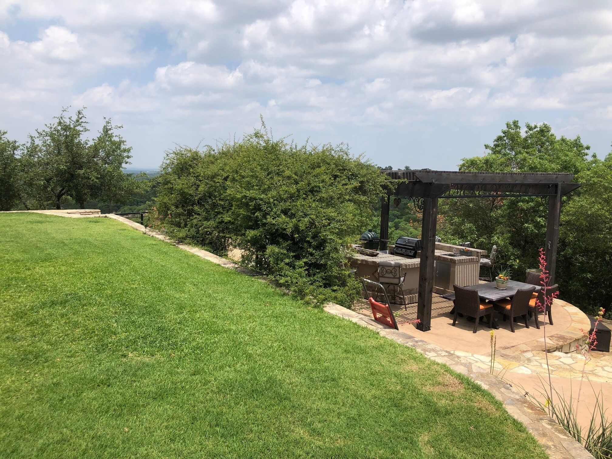 Un patio con una parrilla y zona de estar, rodeado de césped y árboles.