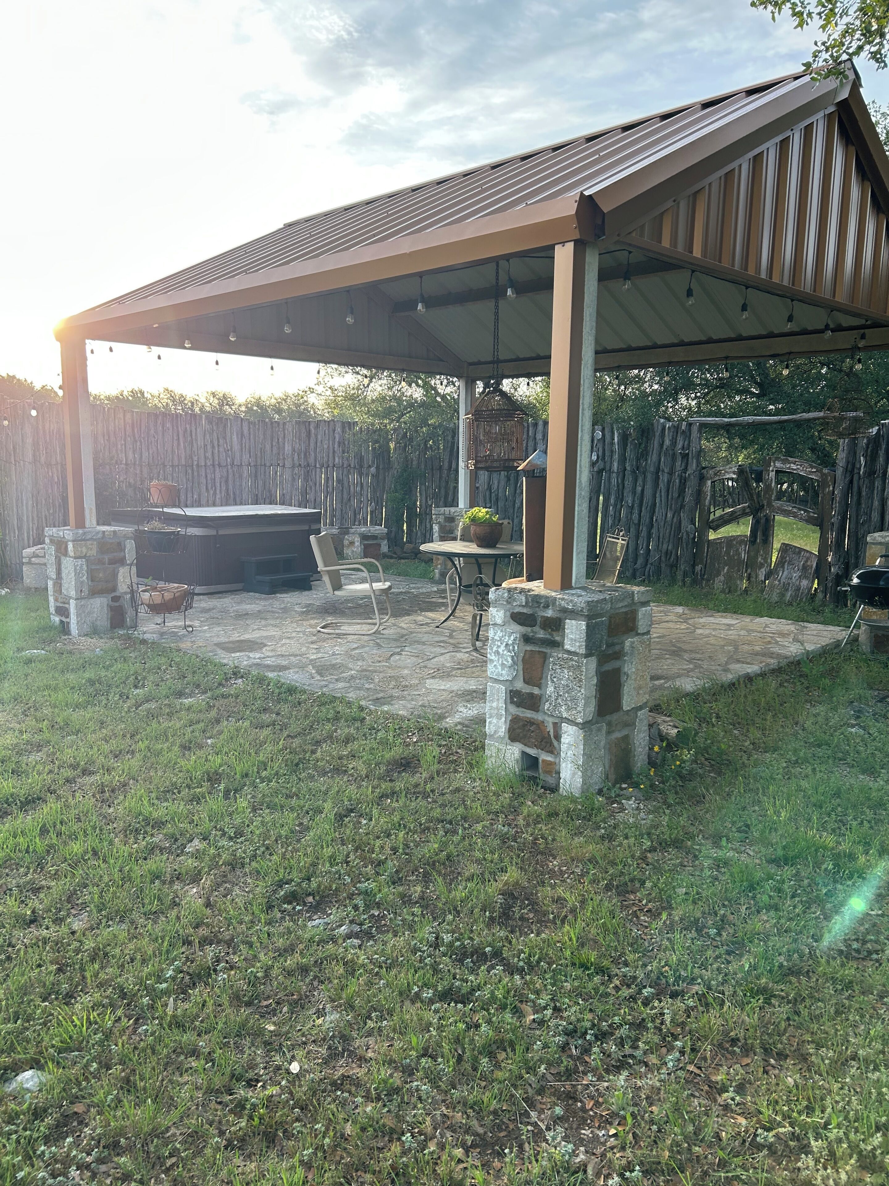 A covered outdoor patio with stone pillars, a barbecue grill, and a table with chairs.