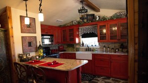 A kitchen with red cabinets, a granite countertop, and a central island with bar stools. - Love of the View  - Glen Rose Luxury Cottage (Glen Rose)