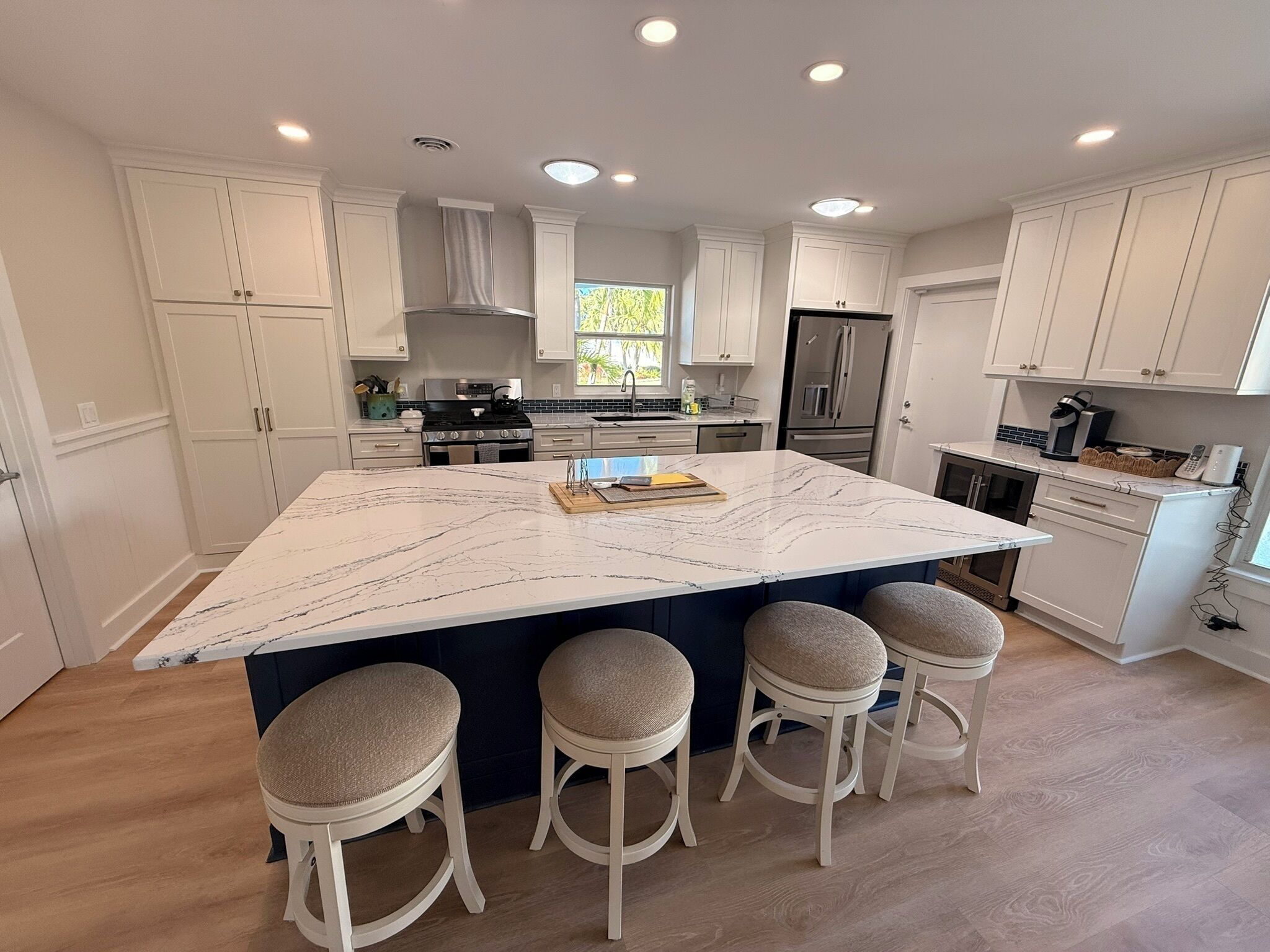 A modern kitchen with white cabinetry, a large marble island with bar stools, and built-in appliances.