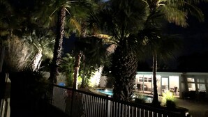 A nighttime view of a pool area with palm trees and a building in the background. - A Shore Thing - Relaxing Island Living , Large Heated Pool, Boat Lift (Holmes Beach)