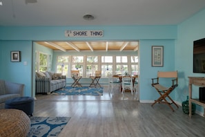 Un soggiorno con una parete blu, un cartello con la scritta "IT'S SHORE THING", un divano, un tavolino da caffè e un'area pranzo con sedie e un tavolo.