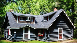 A log cabin with a steeply pitched roof, a front porch, and a chimney. - Rustic two-story log cottage, River-view, Pet-friendly, Downeast Maine (Edmunds Township)