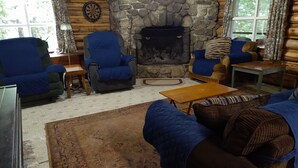 A cozy log cabin interior with a stone fireplace, blue upholstered furniture, and a dartboard on the wall. - Rustic two-story log cottage, River-view, Pet-friendly, Downeast Maine (Edmunds Township)