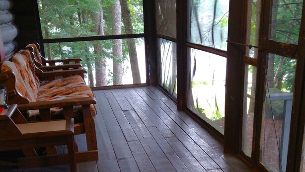 A wooden deck with a bench and a table, overlooking a forested area. - Rustic two-story log cottage, River-view, Pet-friendly, Downeast Maine (Edmunds Township)