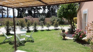 Ein überdachter Patio-Bereich mit Tisch und Stühlen, umgeben von einem gepflegten Garten mit verschiedenen Pflanzen und Blumen.