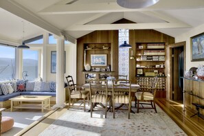 A dining area with a wooden table and chairs, a bookshelf, and a view of the outdoors. - Mermaid's House (Admiral's Quarters) - Tomales Bayfront, Point Reyes, Marshall (Marshall)
