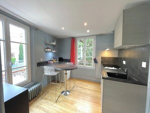A modern kitchen with a bar area, a window with a red curtain, and a view of greenery outside.