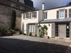 Un bâtiment à deux étages, doté d’une façade en pierre, de volets et d’une cour pavée.