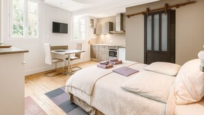 Quarto moderno com cama, mesas de cabeceira, escrivaninha e cozinha compacta.