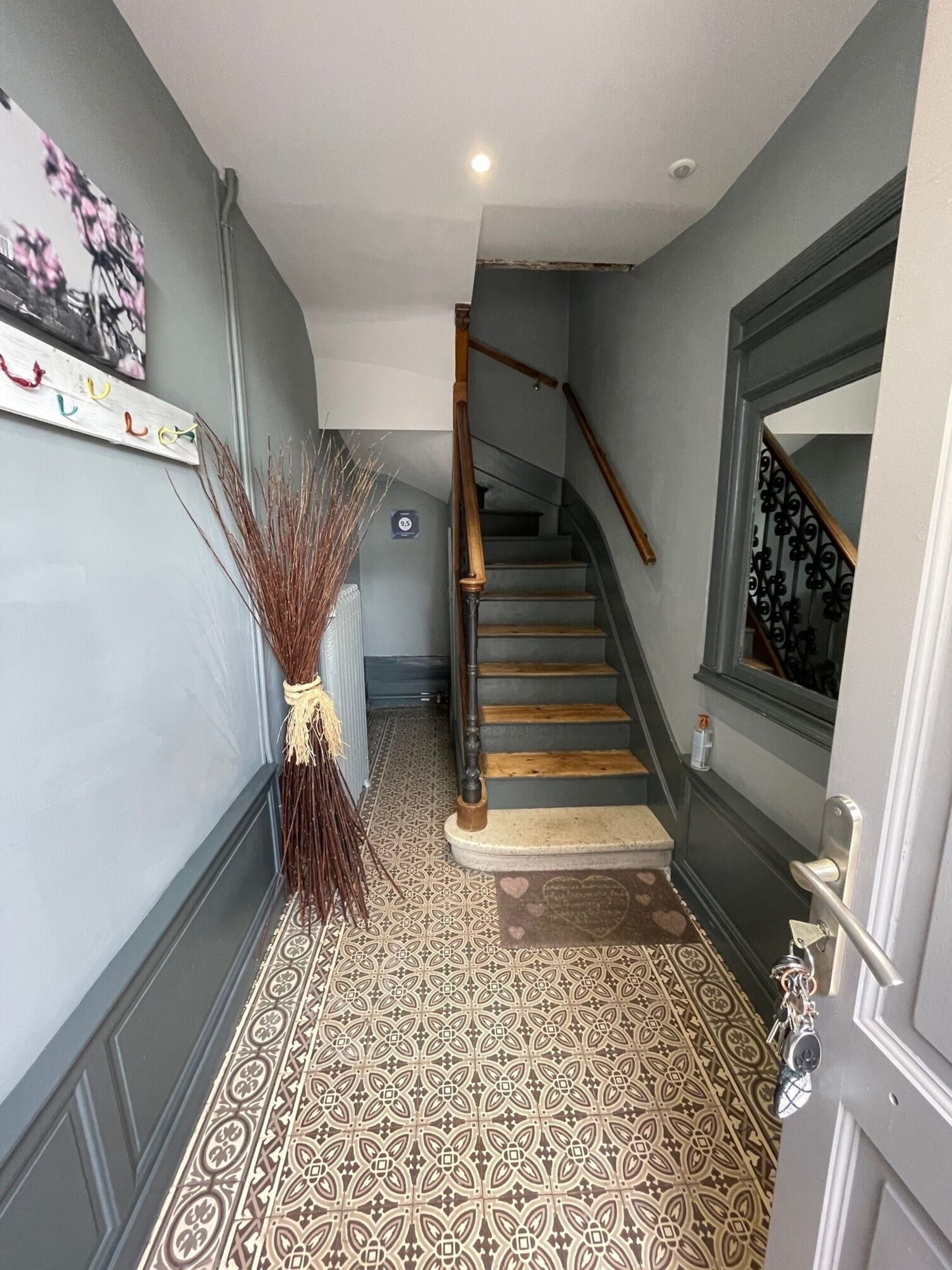 A staircase with a wooden handrail and patterned floor tiles leading to a landing.