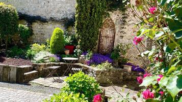 A garden with a stone wall, a wooden gate, and various plants including roses.