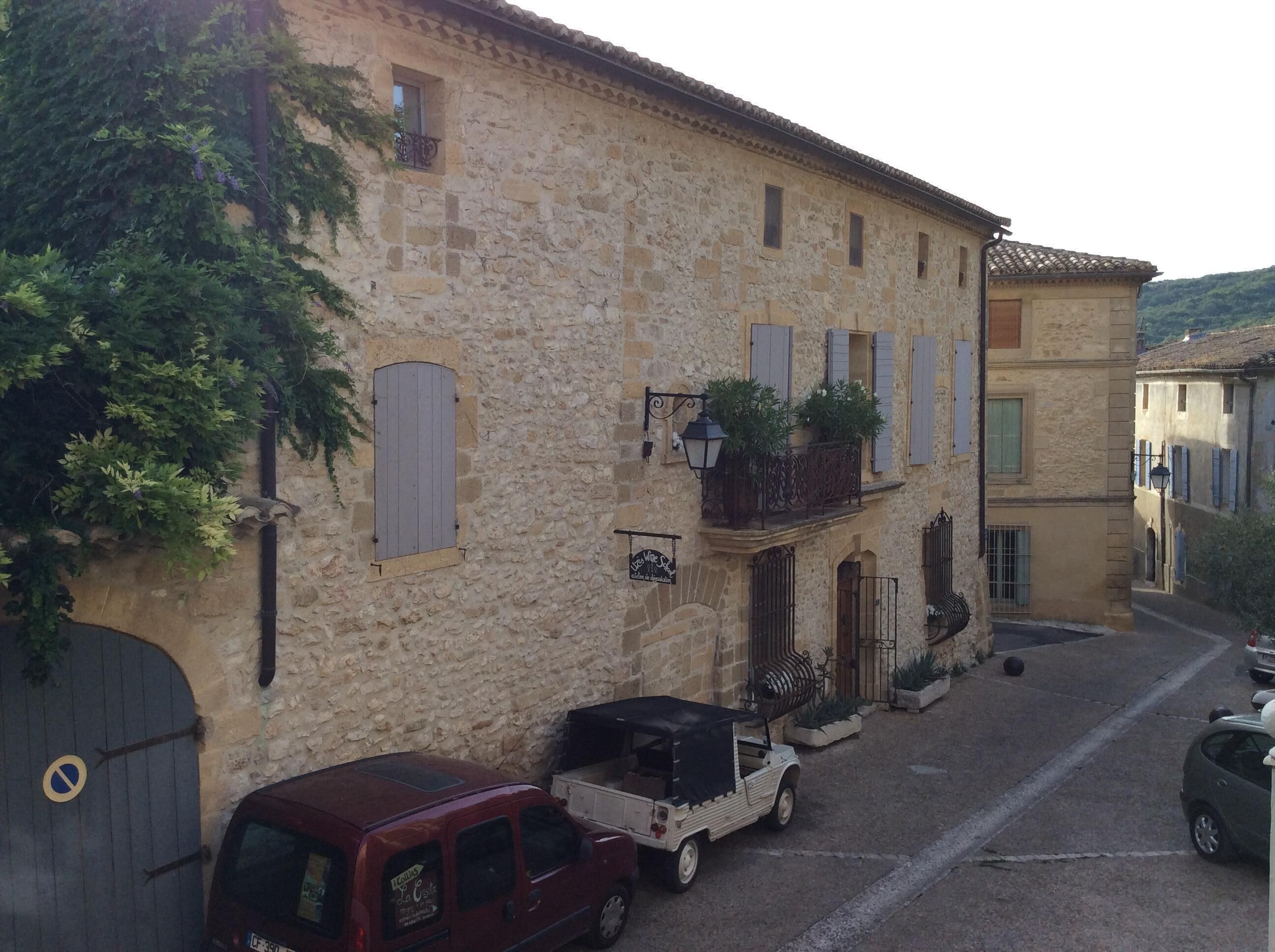 A stone building with a narrow street, parked vehicles, and a sign indicating a restaurant.