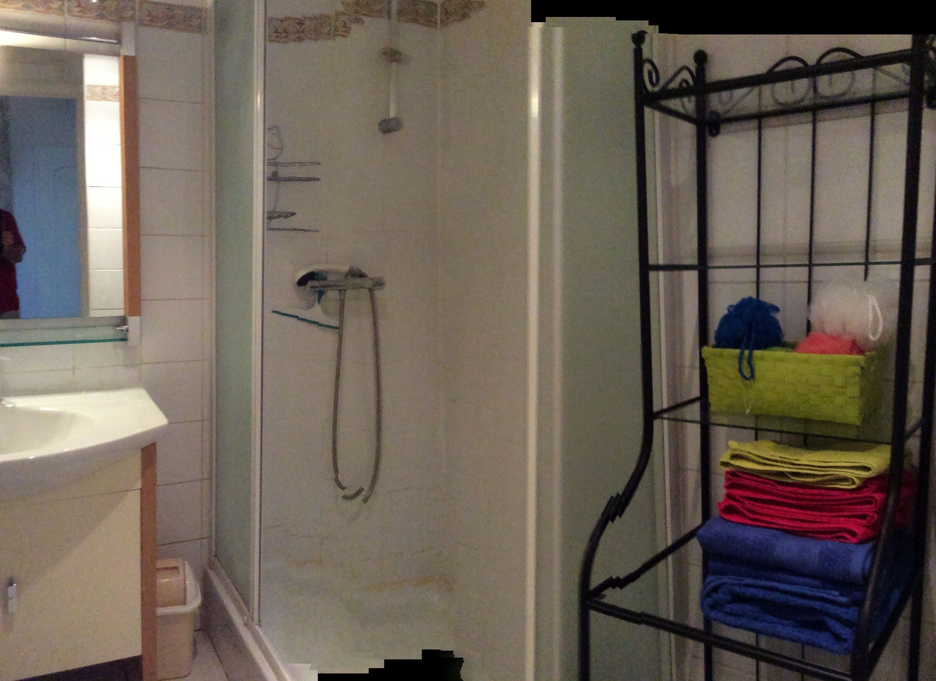 A bathroom with a shower, a sink, and a towel rack with folded towels.