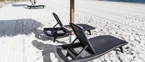 A beach with two sun loungers and a thatched umbrella.
