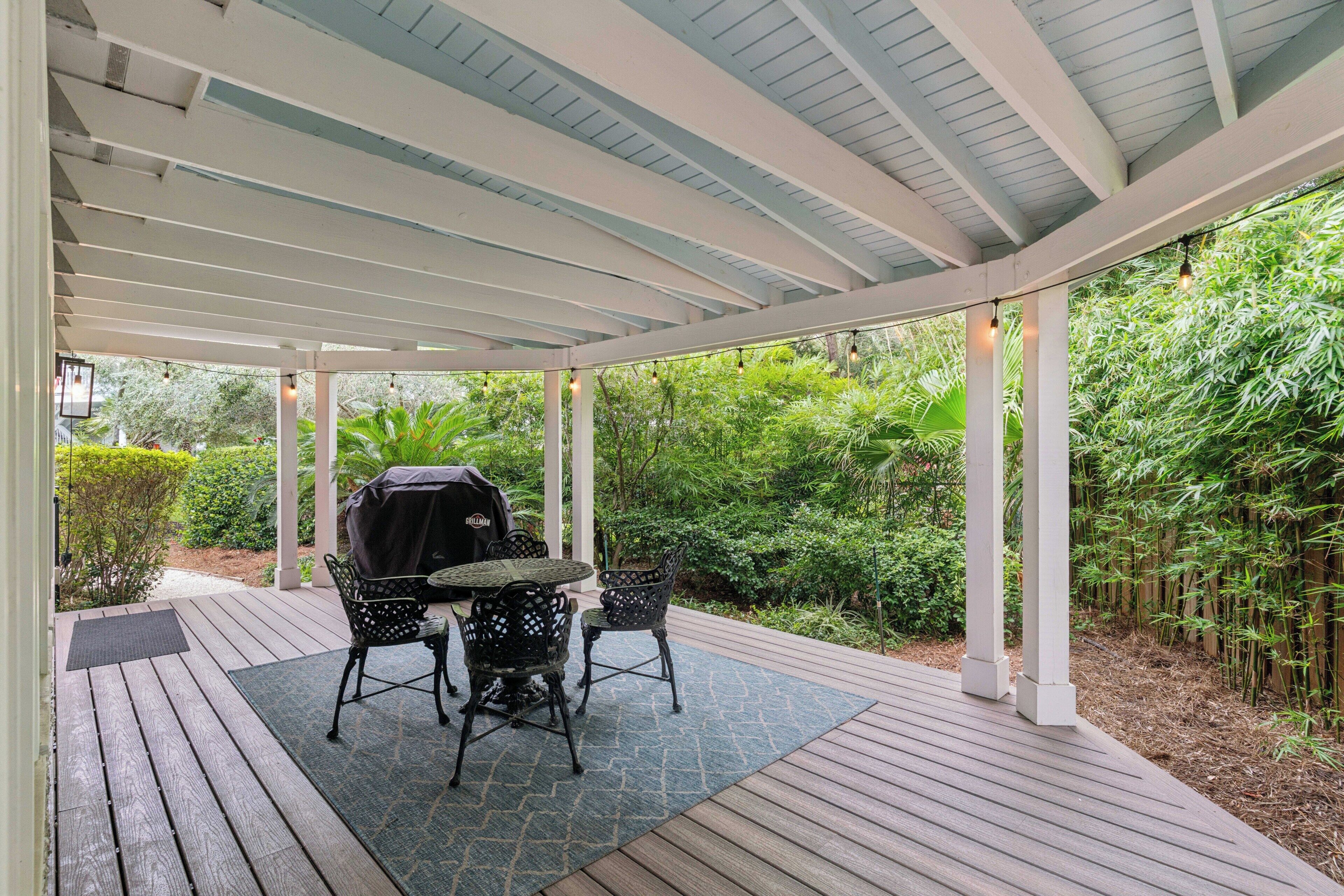 A covered outdoor patio with a grill, chairs, and a table.