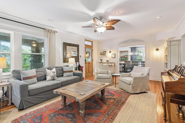 A spacious living room with a grey sofa, a wooden coffee table, and a piano.