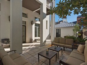 Relax in a spacious outdoor area with a seating arrangement, sofa, and tables, surrounded by plants and offering a view of the surrounding buildings.