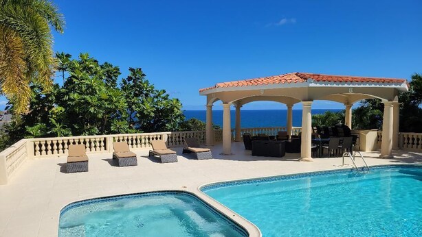A pool with a hot tub, lounge chairs, and a covered seating area with a view of the ocean.