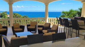 A covered outdoor seating area with wicker furniture and a view of the ocean.