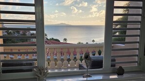 A bathroom with a bathtub, a window with a view of the sea, and a balcony with a railing.