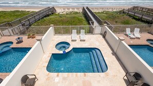 Un área de piscina en la azotea con dos piscinas, sillas de descanso y vista a la playa.