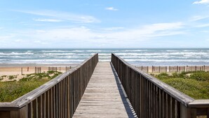 Pasarela de madera que conduce a una playa, con olas al fondo.