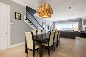 A dining area with a dark wooden table and beige chairs, a staircase with black railings, and a large window offering a view of the sky. - Gulf Breeze: Oceanfront Home with Private Pool & Direct Beach Access! (South Padre Island)