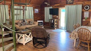 Interior acogedor de una cabaña con detalles de madera, un sofá, una mesa de comedor, un televisor y una chimenea.