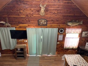 Ein rustikales Blockhaus-Interieur mit Holzwänden, einem aufgehängten Hirschkopf, einem Fisch an der Wand und einem Tisch mit kariertem Tischläufer.