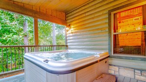 Uma cabana de madeira com hidromassagem em um deck, rodeada por árvores.