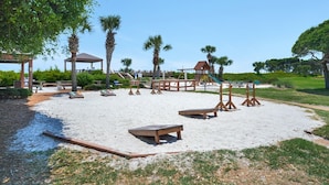 Ein Spielplatz mit Sand, Palmen und einem Pavillon.