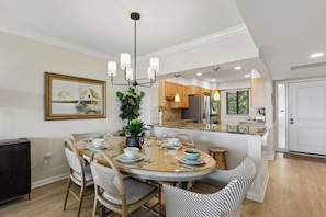 A dining area with a round table, chairs, a chandelier, and a kitchen in the background.