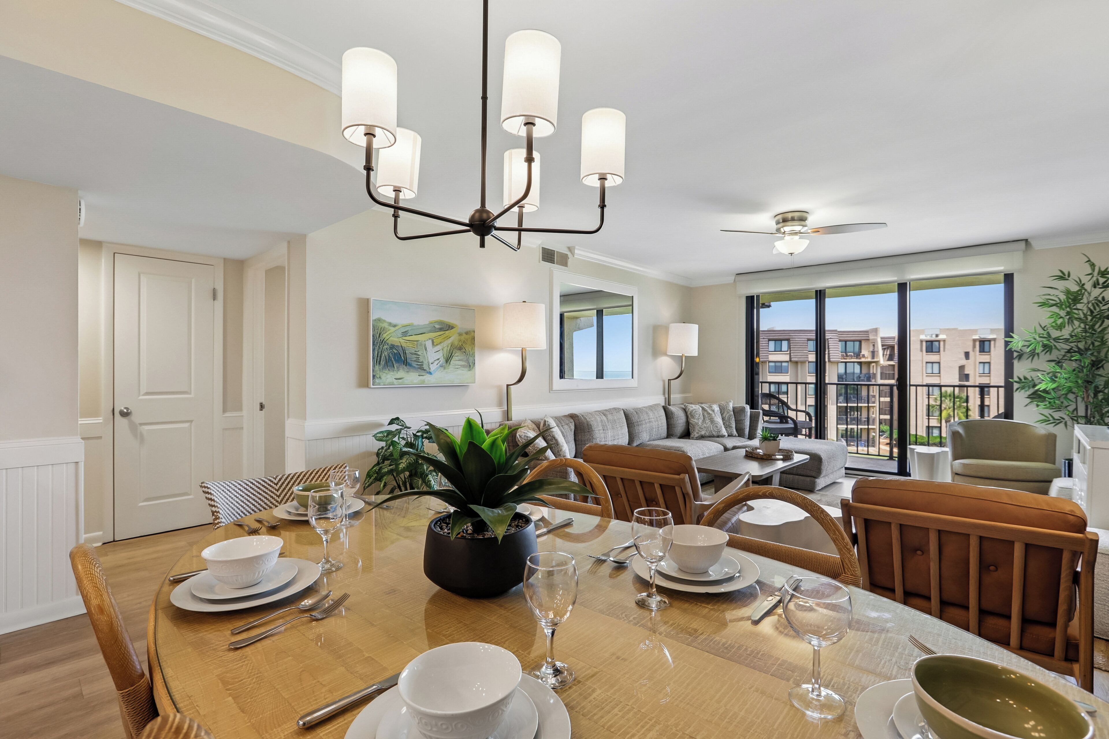 Ein Essbereich mit einem Holztisch, gedeckt für vier Personen, umgeben von Stühlen. Über dem Tisch hängt eine Chandelier und im Hintergrund ist ein Deckenventilator zu sehen.