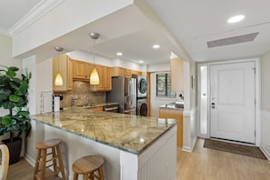 A modern kitchen with a large island, wooden cabinets, stainless steel appliances, and pendant lighting.
