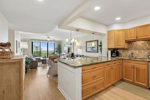A modern kitchen with wooden cabinets, a marble countertop, and a dining area with a view.