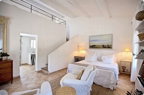 A bedroom with a bed, two bedside tables, a chair, a staircase, and a painting on the wall. - Gorgeous in Gordes, Elegantly Furnished with Pool, Tennis and Views  (Gordes)