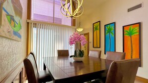 Un comedor con una mesa de madera, sillas, un jarrón con flores y obras de arte en las paredes.