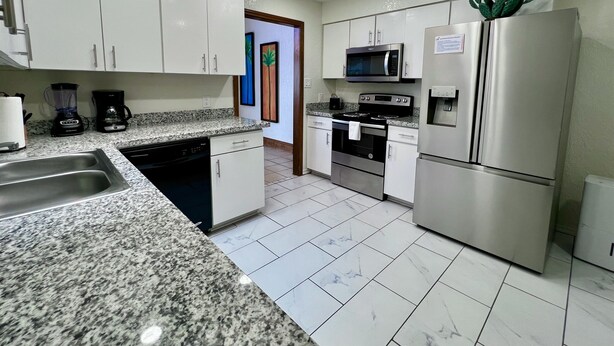 Una cocina moderna con armarios blancos, encimeras de granito y electrodomésticos de acero inoxidable, además de un dispensador de agua.
