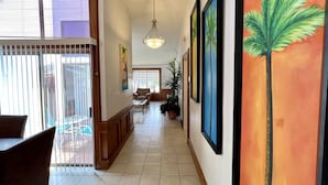 Un pasillo con suelo de baldosas, un comedor con sillas y una mesa, y un cuadro grande de una palmera en la pared.