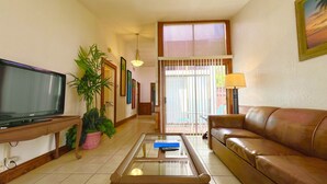 Una sala de estar con televisión, un sofá, una mesa de centro y una planta en maceta.