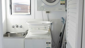 Ein kleiner Hauswirtschaftsraum mit Waschmaschine, Wäscheständer und einem Fenster mit Blick ins Freie.