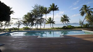 A wooden deck with a clear view of a swimming pool and palm trees.