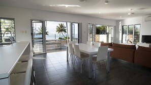 A modern kitchen with a dining area, a sofa, and large sliding glass doors leading to a balcony with a view of the sea.