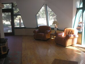 Ein Zimmer mit zwei Ledersesseln, einem kleinen Tisch mit Lampe und großen Fenstern mit Blick auf Bäume und eine Straße.