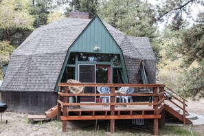 Eine Hütte mit einem grünen Dach, einer Holzterrasse und einer Sitzgruppe.