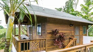 A wooden cabin with a wooden deck, a covered porch, and a small window.